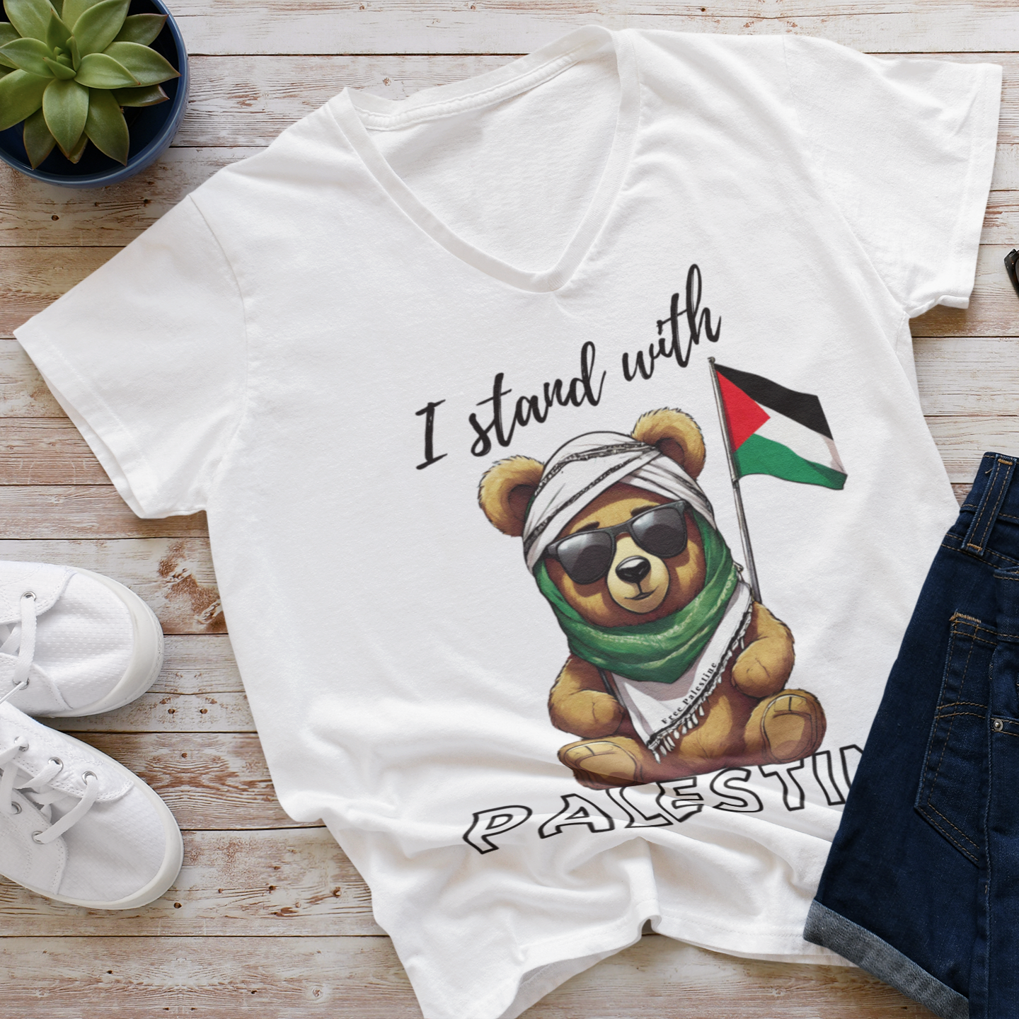 White t-shirt with a bear graphic and text on a wooden surface with shoes and sunglasses.