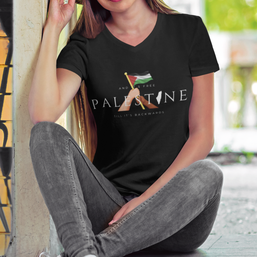 Person wearing a t-shirt with 'Palestine' text sitting against a graffiti-covered wall.