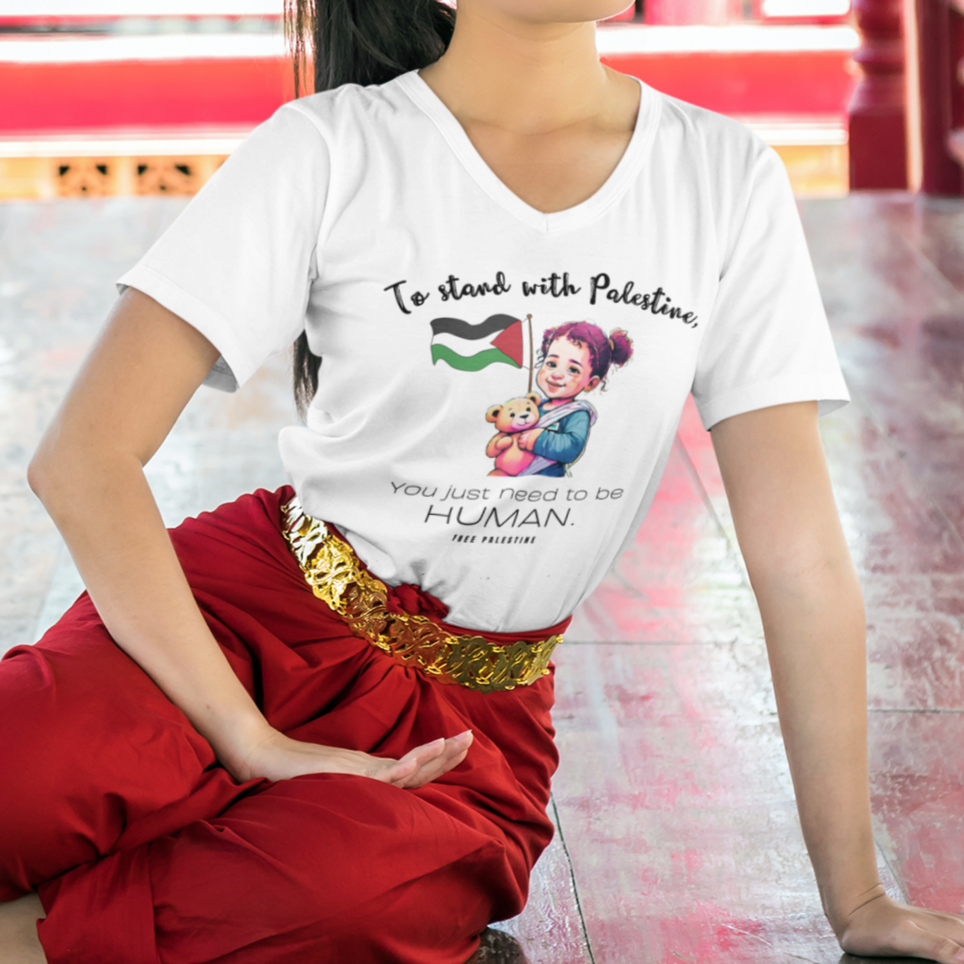 Woman sitting on a wooden floor wearing a white t-shirt with a graphic design and red pants.