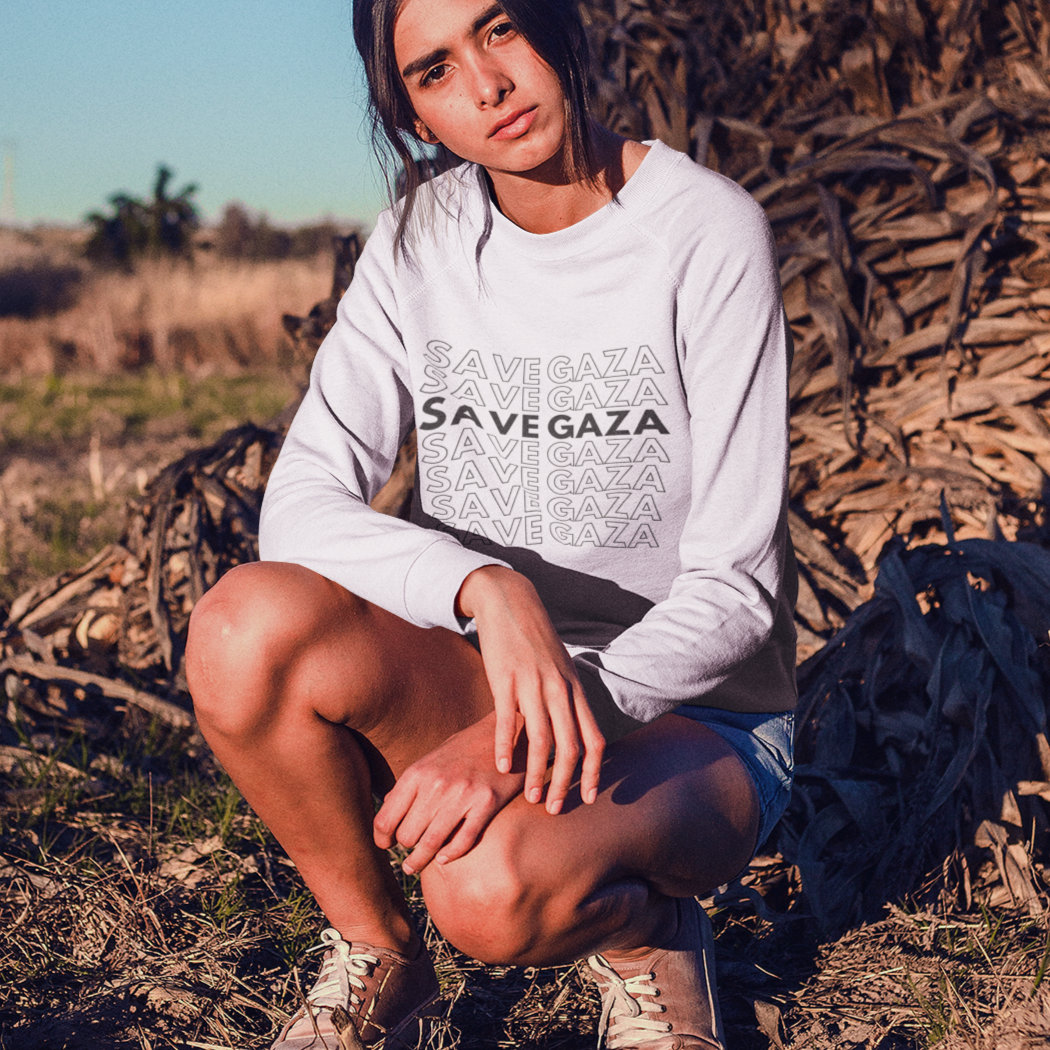 Person wearing a 'Save Vegaza' sweatshirt sitting in a field with dry plants.