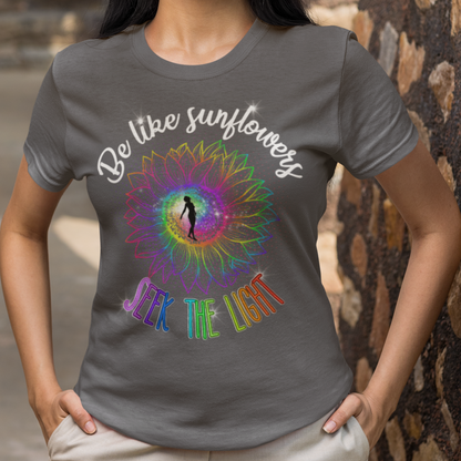 Woman wearing a gray t-shirt with a colorful design and text, standing against a stone wall.