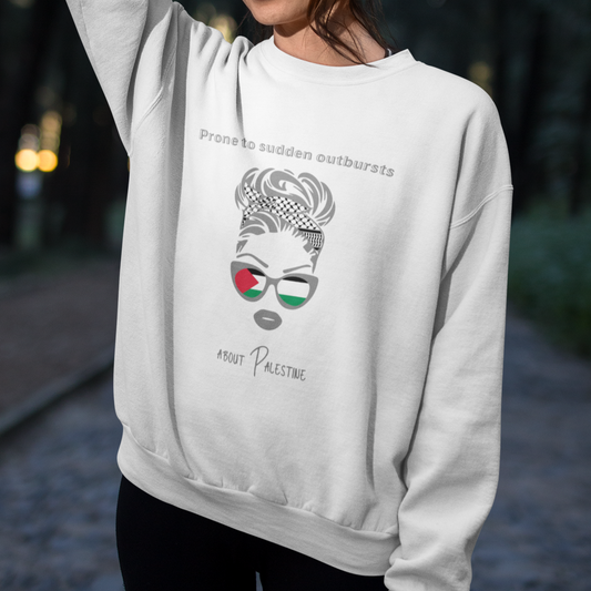 Woman wearing a white sweatshirt with a graphic design and text, standing outdoors.