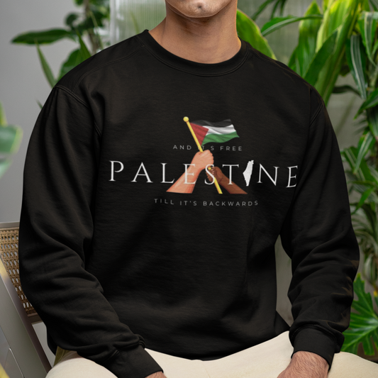 Person wearing a black sweatshirt with a flag design and text, sitting among plants.