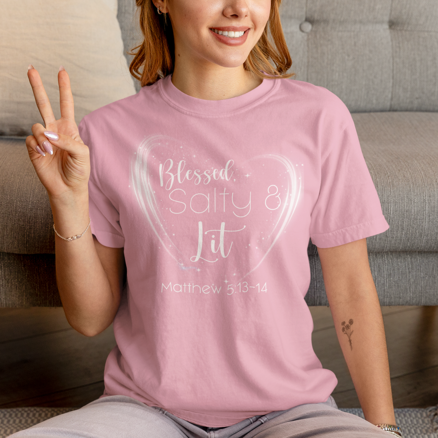 Person wearing a pink t-shirt with text, sitting on a couch.