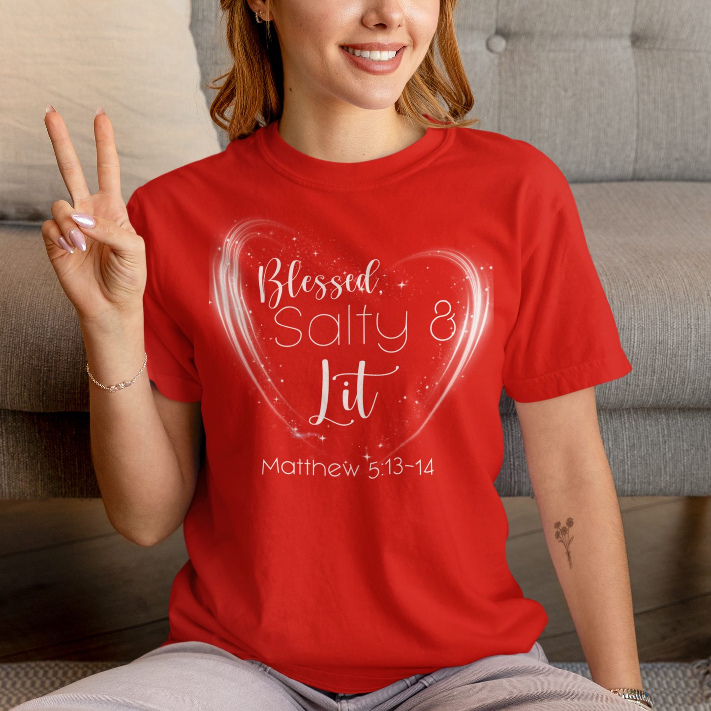 Person wearing a red t-shirt with a heart design and text, sitting on a couch.