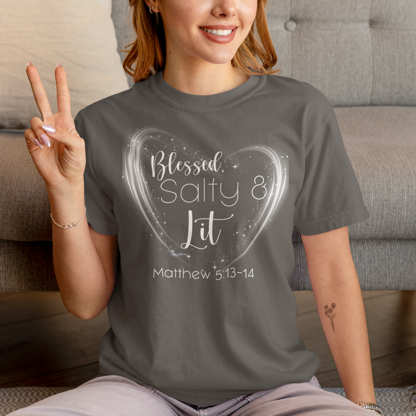 Person wearing a gray t-shirt with 'Blessed, Salty & Lit' design, sitting on a couch.