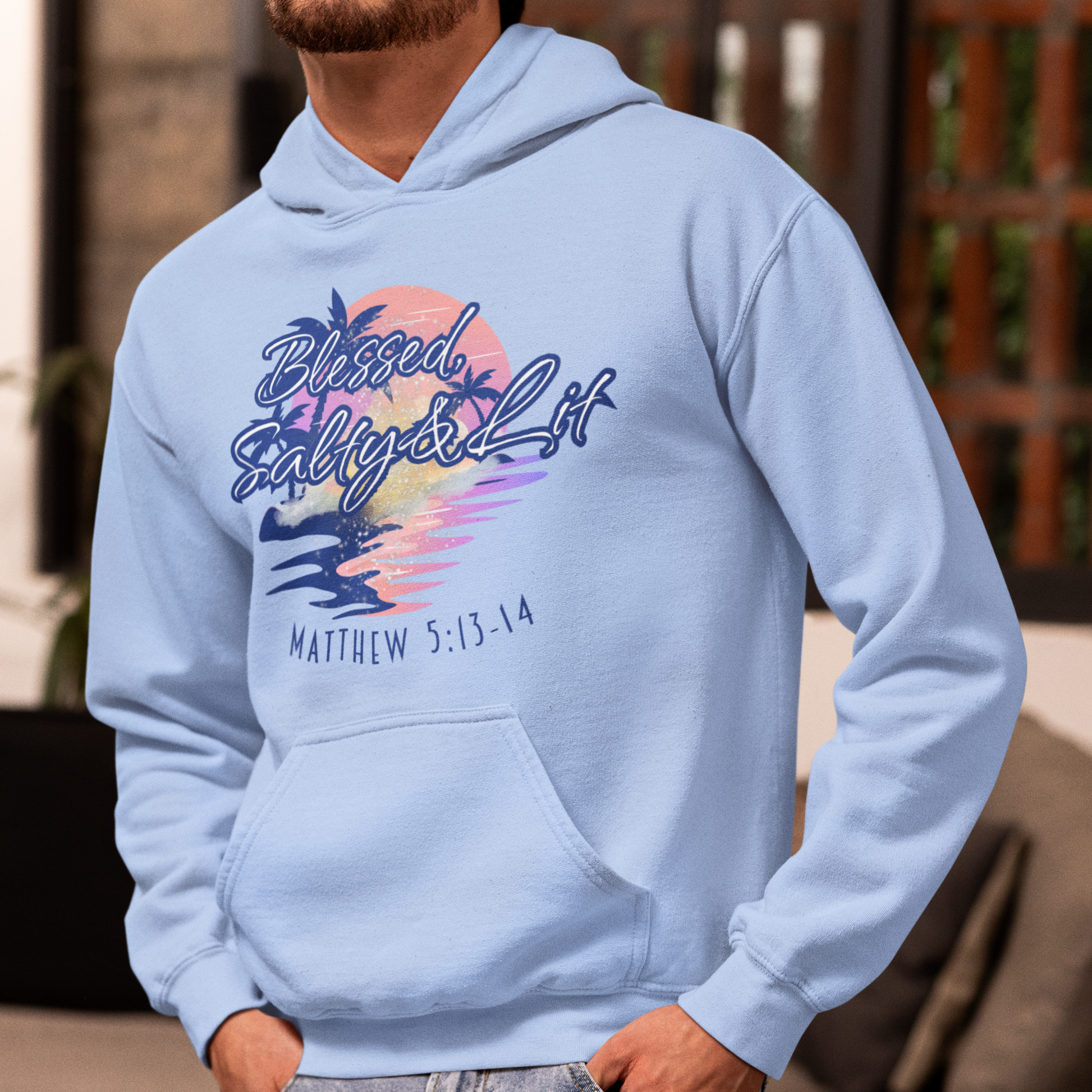 Man wearing a light blue hoodie with a colorful design and text, standing outdoors.