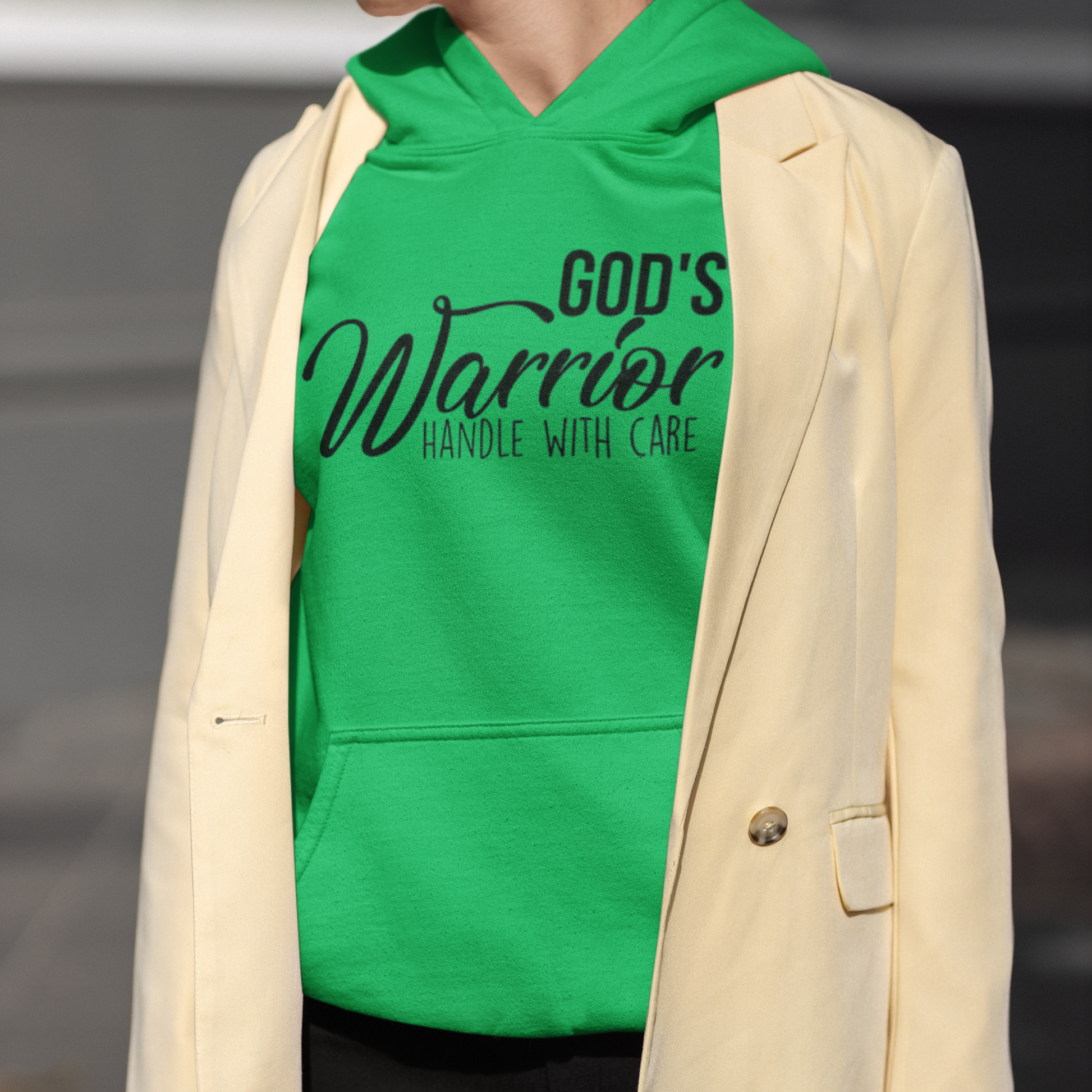 Person wearing a green hoodie with 'God's Warrior Handle with Care' text and a beige blazer.