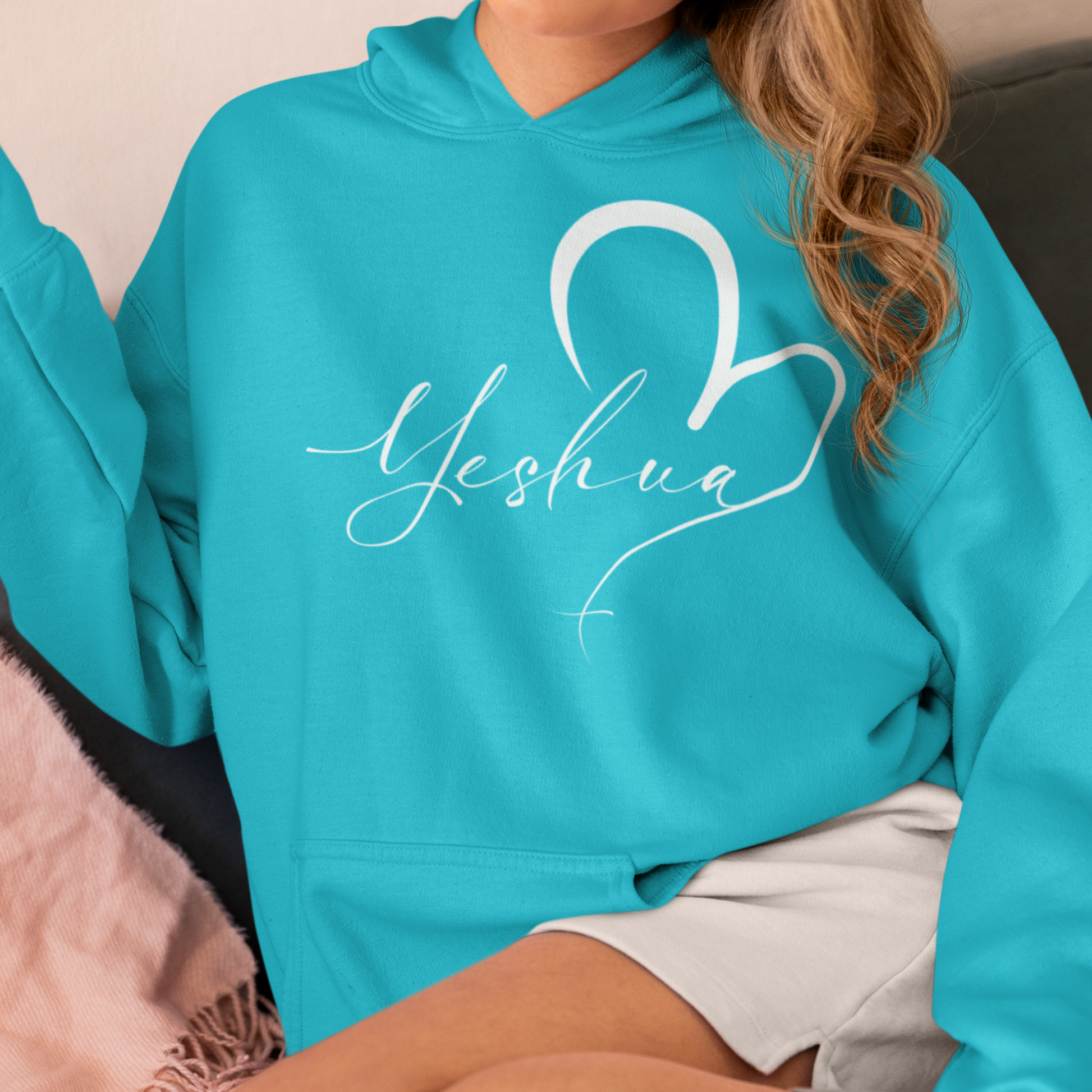 Person wearing a turquoise hoodie with 'Yeshua' and a heart design.
