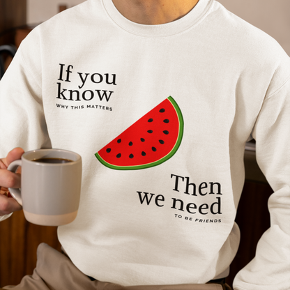 Person wearing a white sweatshirt with a watermelon graphic and text, holding a mug.