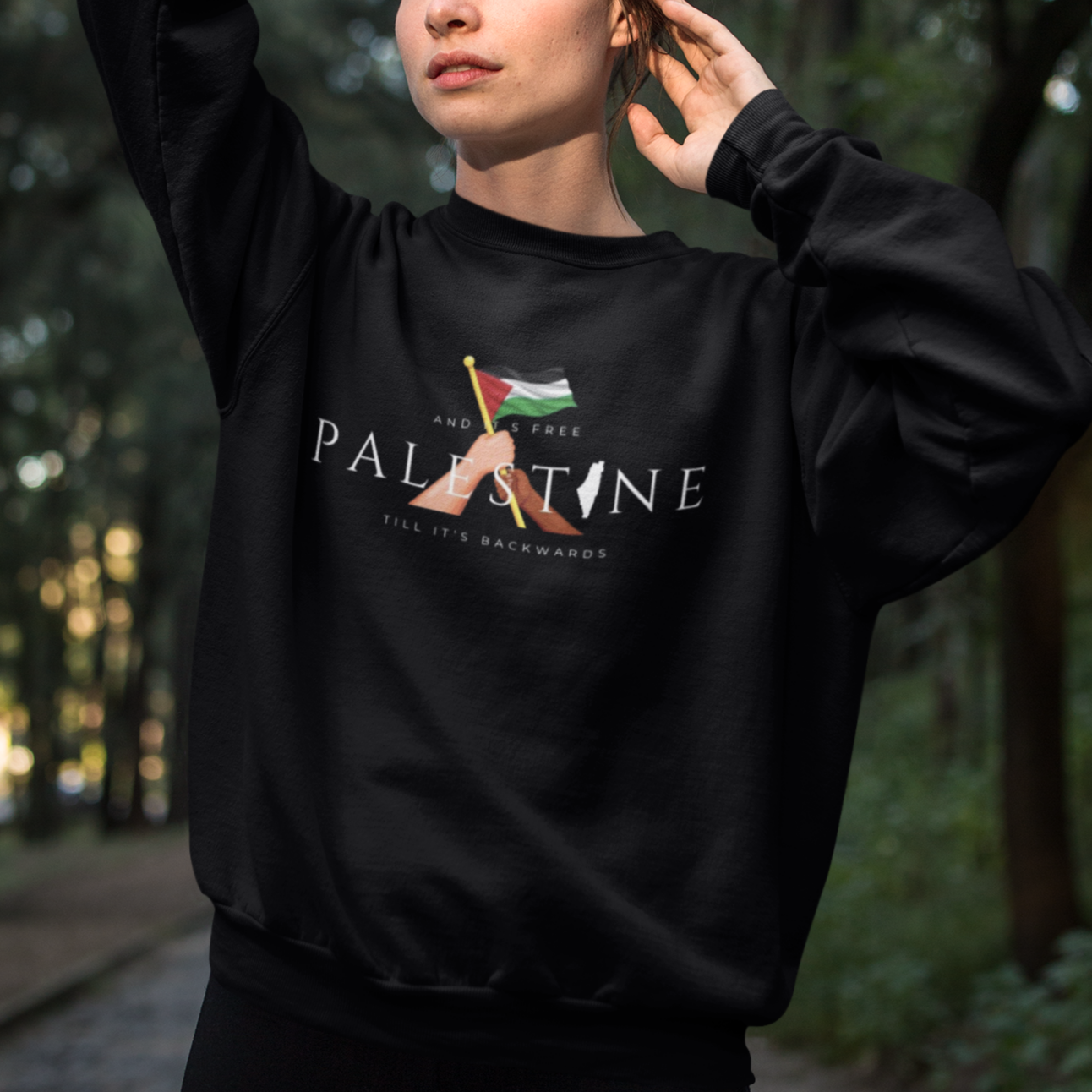Person wearing a black sweatshirt with a design and text in a forest setting