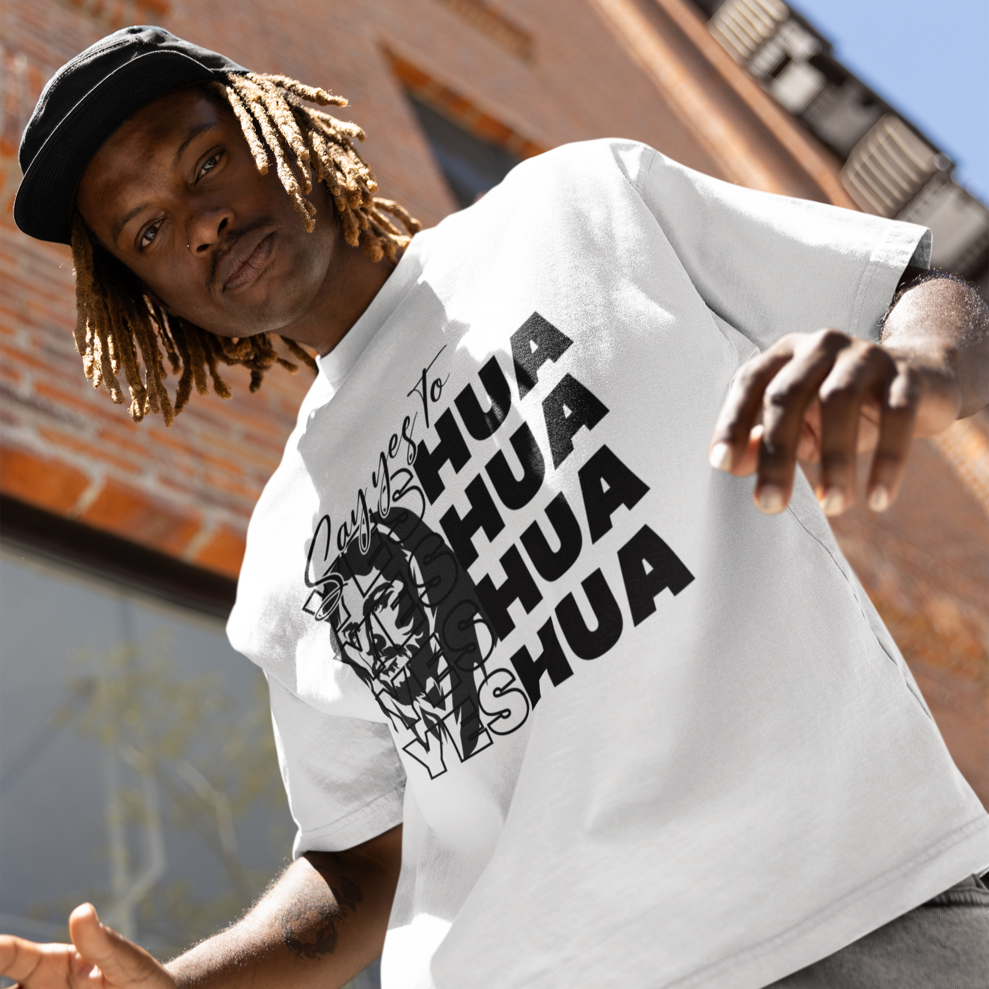 Person wearing a white t-shirt with black text and graphics, standing against a brick building.