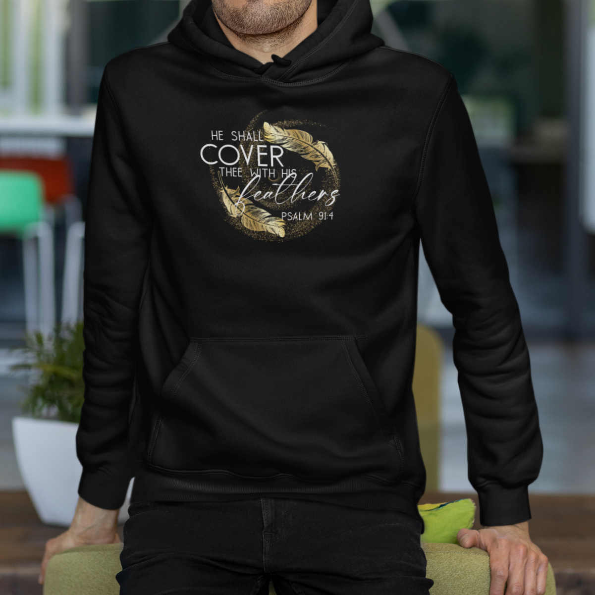 Man wearing a black hoodie with text and graphics, standing indoors.