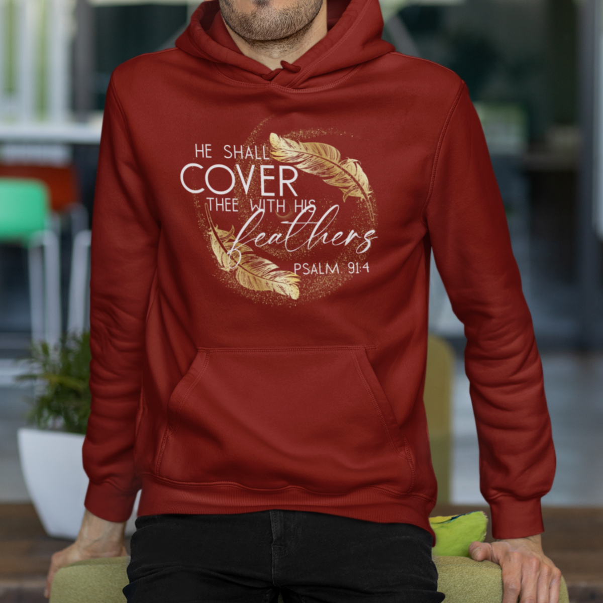 Man wearing a red hoodie with text and design, sitting on a green chair indoors.