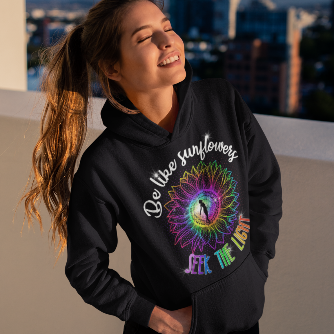 Woman wearing a black hoodie with colorful design and text, standing on a rooftop with cityscape in the background.