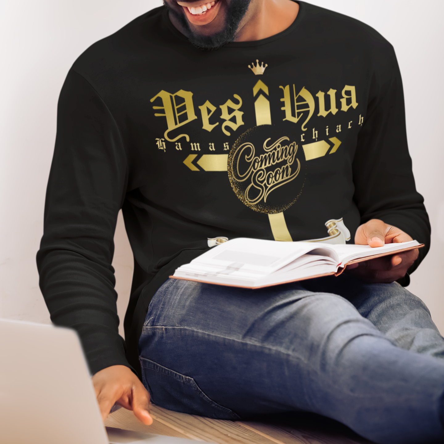 Man wearing a black sweatshirt with gold text, sitting at a desk with a laptop and notebook.