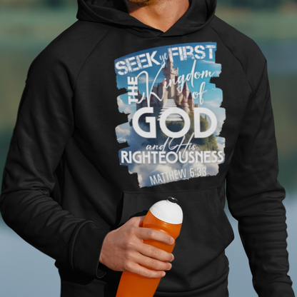 Man wearing a black hoodie with a motivational quote, holding an orange cup outdoors by a lake.