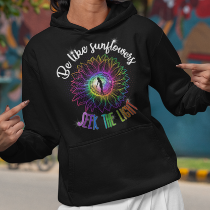 Woman wearing a black hoodie with a colorful design and text, standing in front of a mural.