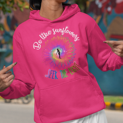 Woman wearing a pink hoodie with colorful design and text, standing in front of a colorful mural.