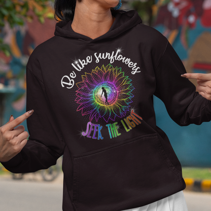 Woman wearing a black hoodie with a colorful design and text, standing in front of a mural.