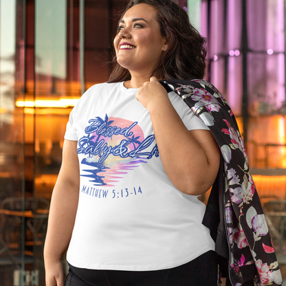 Woman wearing a white t-shirt with colorful text and black pants, standing in front of a building.
