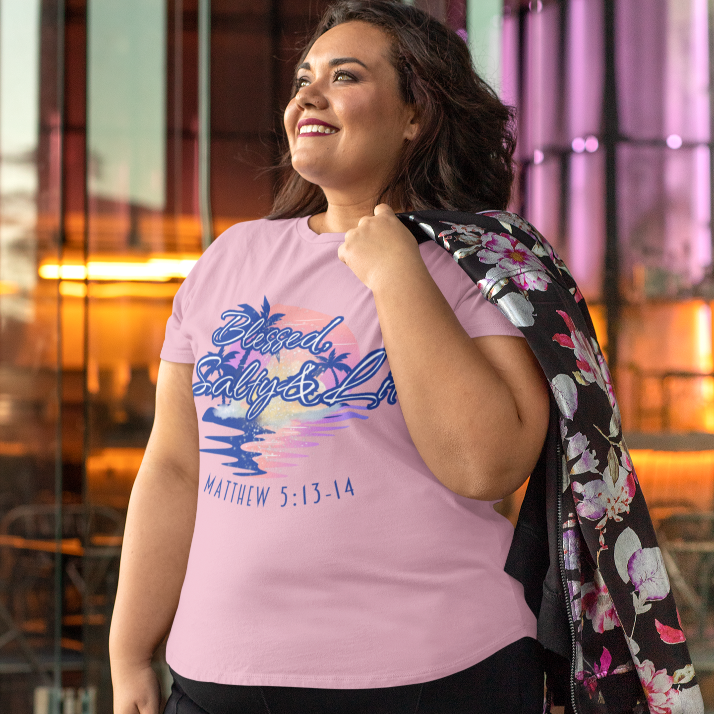 Woman wearing a pink graphic t-shirt with black pants, standing in an urban setting.