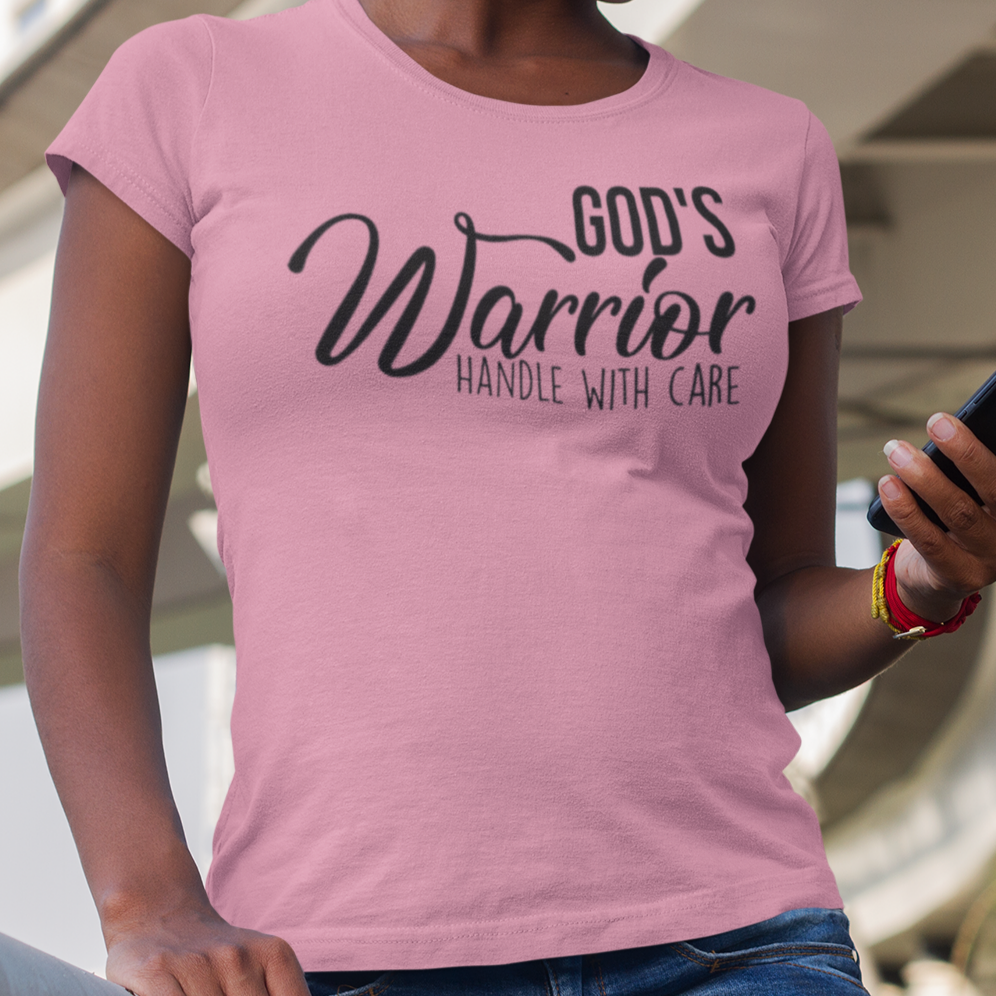 Person wearing a pink t-shirt with 'God's Warrior Handle with Care' text, standing outdoors.