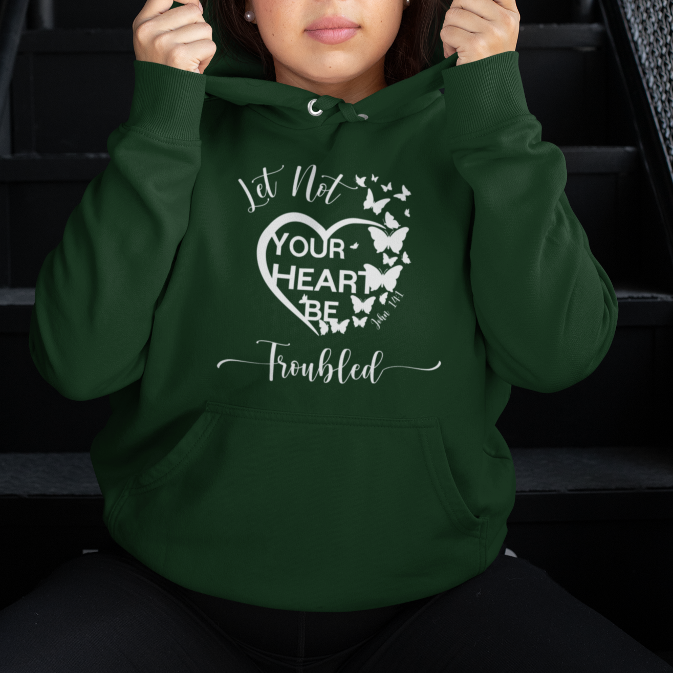 Person wearing a green hoodie with a heart design and text, sitting on stairs.