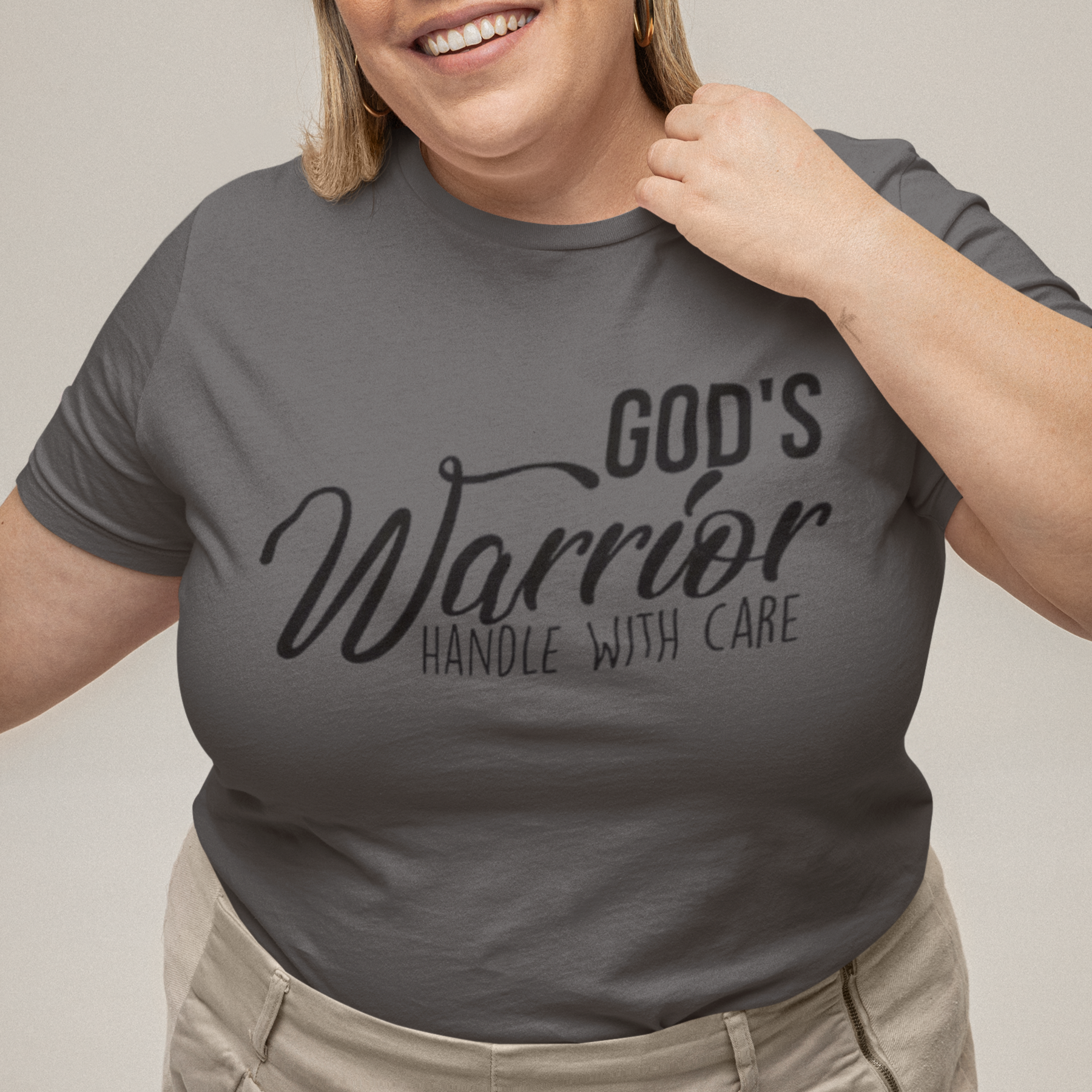 Person wearing a gray t-shirt with 'God's Warrior Handle with Care' text on a plain background