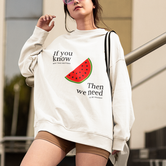 Woman wearing a white sweatshirt with text and a watermelon graphic, standing on steps outdoors.