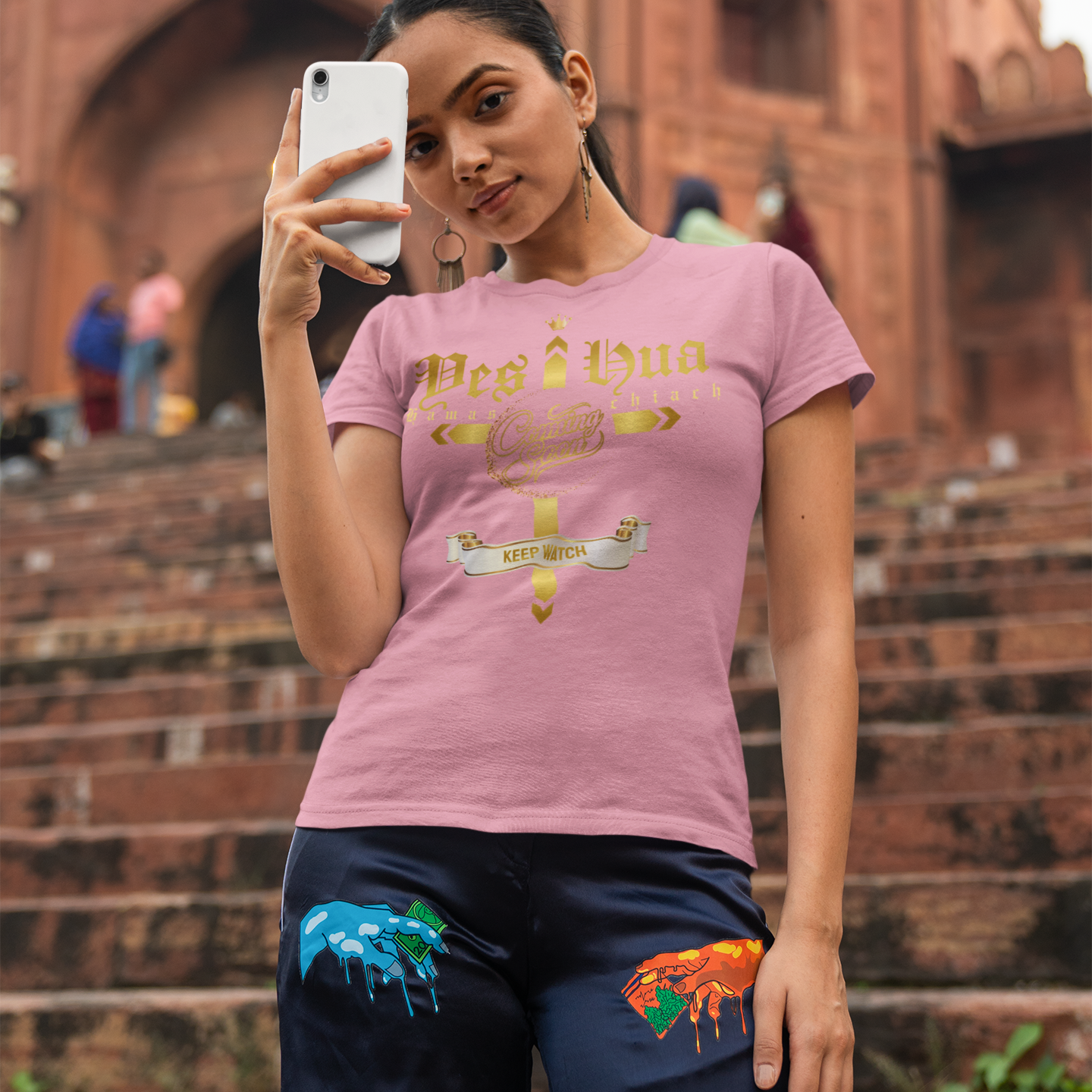 Woman taking a selfie in front of a historic building wearing a pink t-shirt with text and graphics.