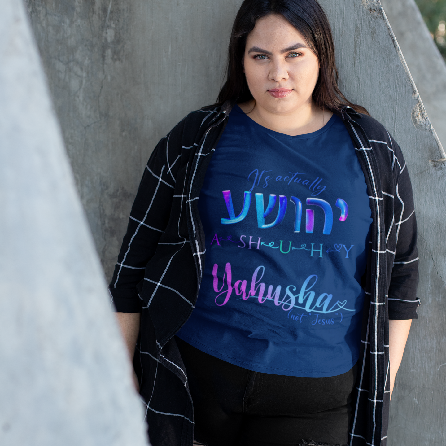 Person wearing a blue t-shirt with colorful text, standing against a concrete wall.