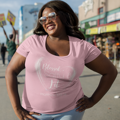 Woman wearing a pink t-shirt with text, standing on a street with palm trees and buildings in the background.