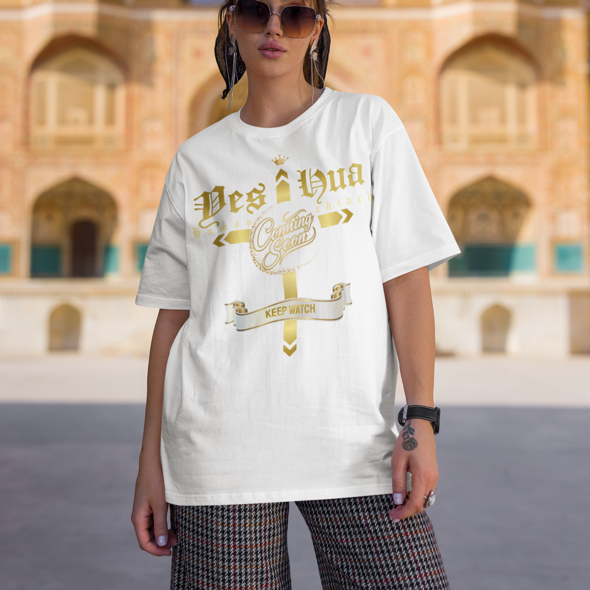 Person wearing a white t-shirt with gold text in front of an architectural building.