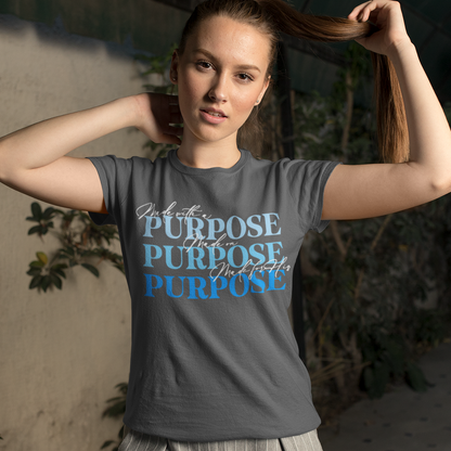 Woman wearing a gray t-shirt with 'Purpose' printed on it, standing against a neutral wall with plants.