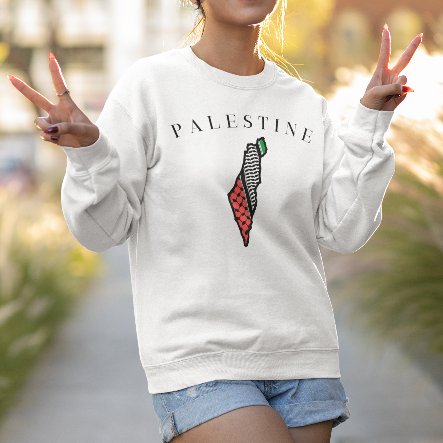 Person wearing a white sweatshirt with a graphic design, making peace signs outdoors.
