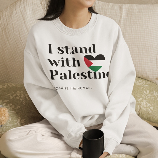 Person wearing a white sweatshirt with 'I stand with Palestine' text, sitting on a couch with a teddy bear.