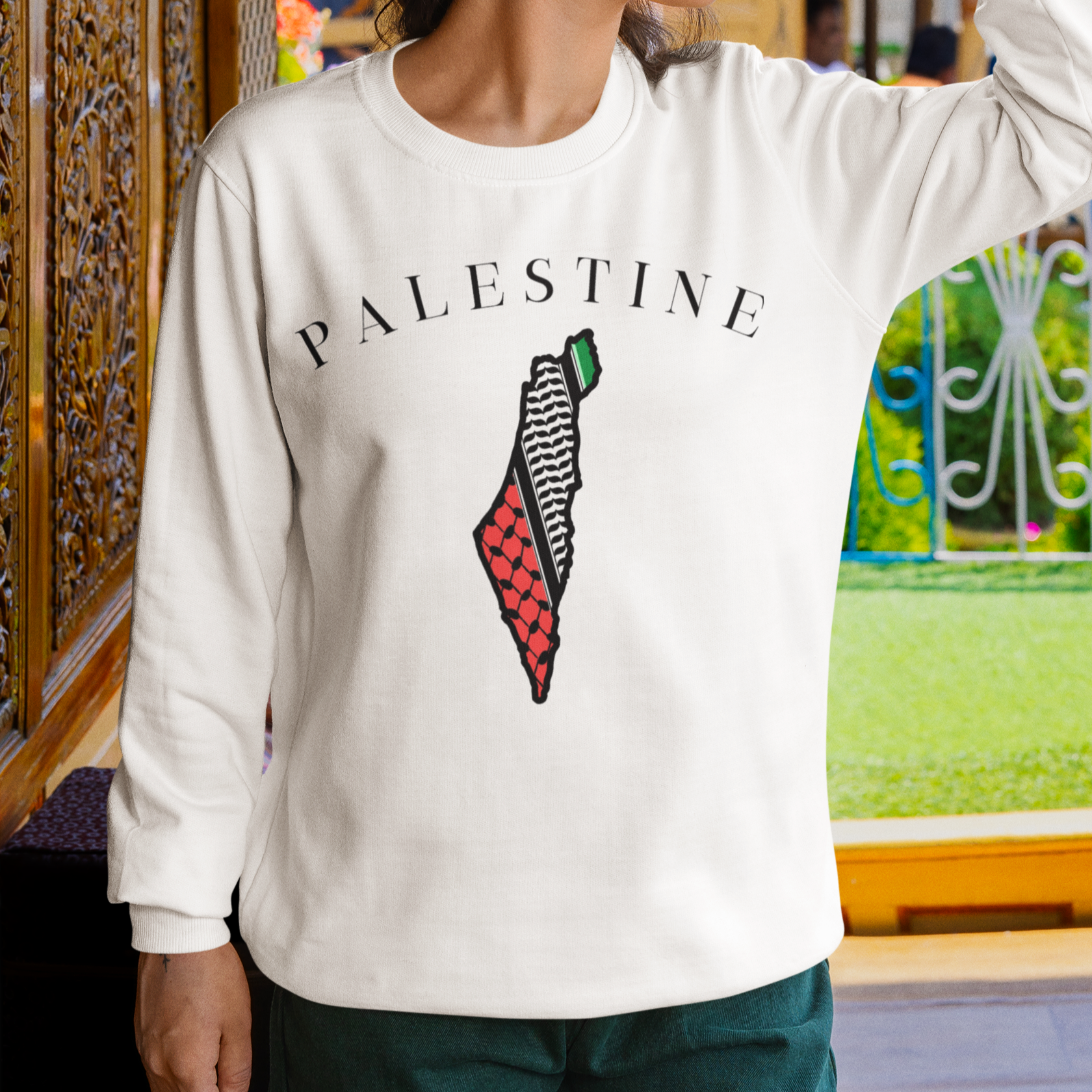 Woman wearing a white sweatshirt with 'PALESTINE' and a map design, standing in an outdoor setting.