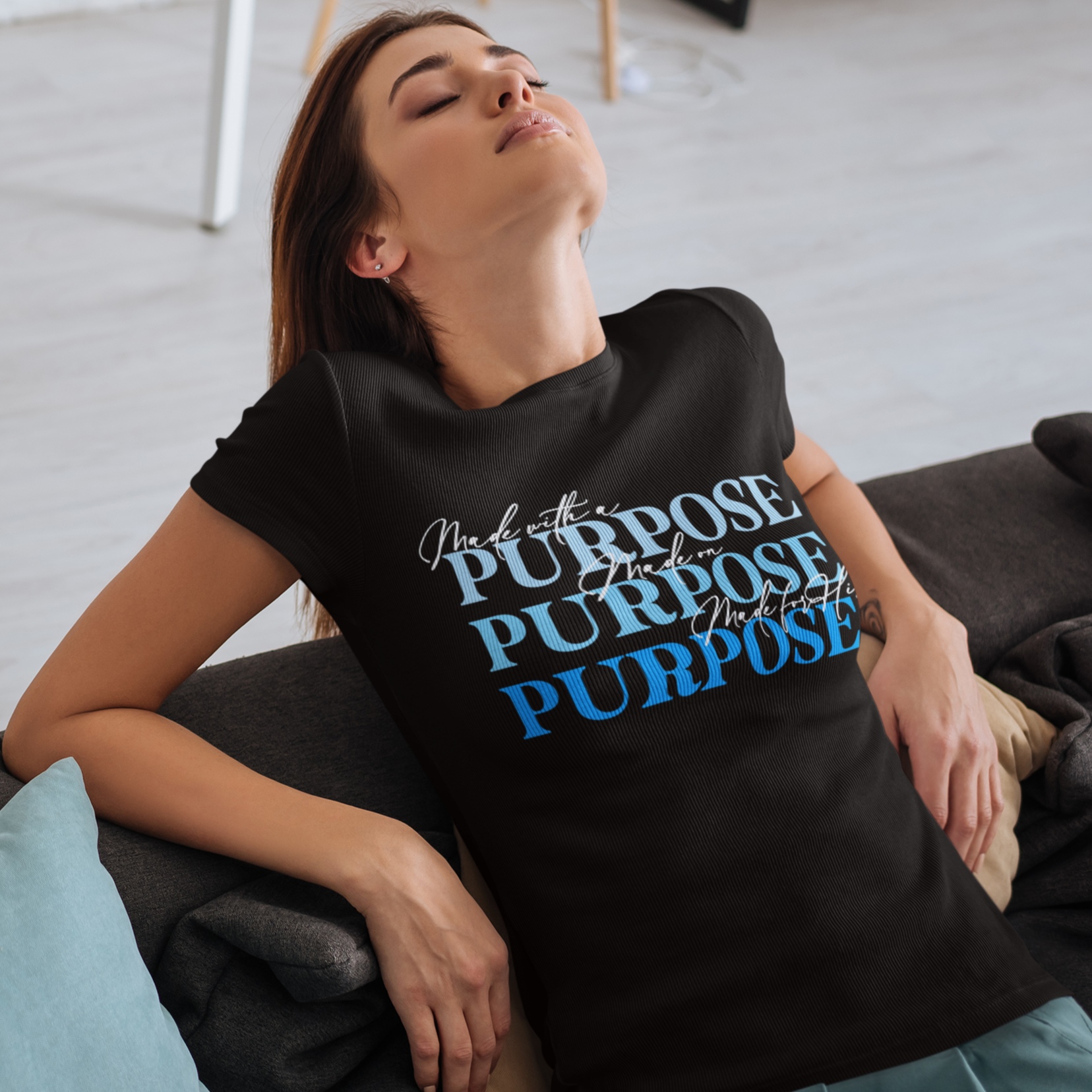 Woman wearing a black t-shirt with 'Purpose' text in different languages, sitting on a couch.