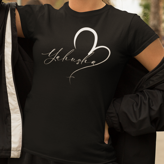 Person wearing a black t-shirt with 'Yahusha' design, holding sunglasses, outdoors.
