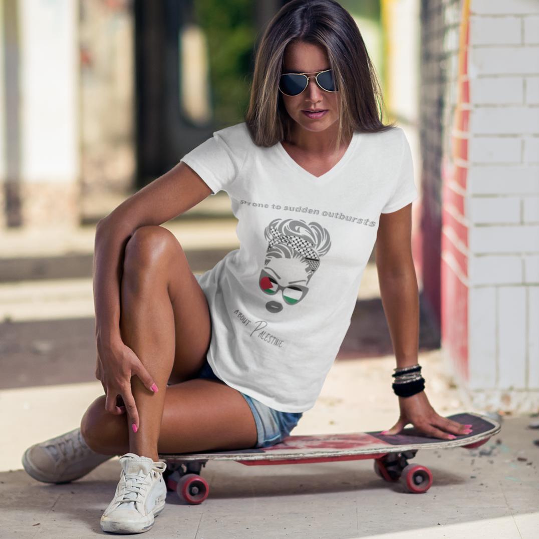 Woman sitting on a skateboard wearing a white t-shirt with a graphic design, sunglasses, and denim shorts in an urban setting.