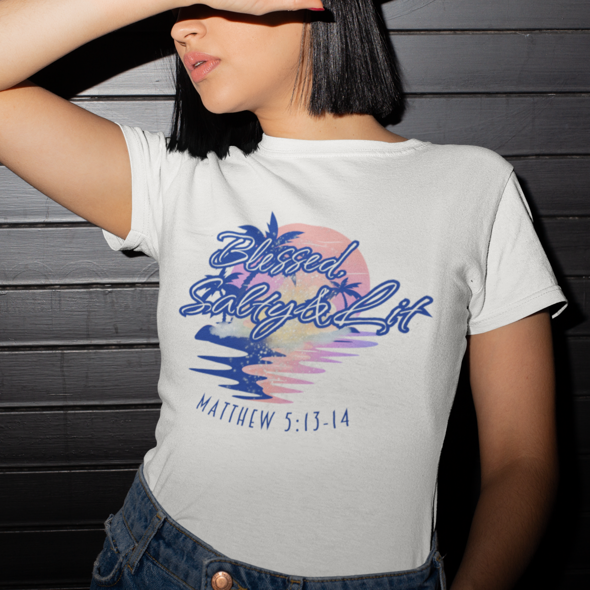Person wearing a white t-shirt with colorful graphic and text against a dark wooden background