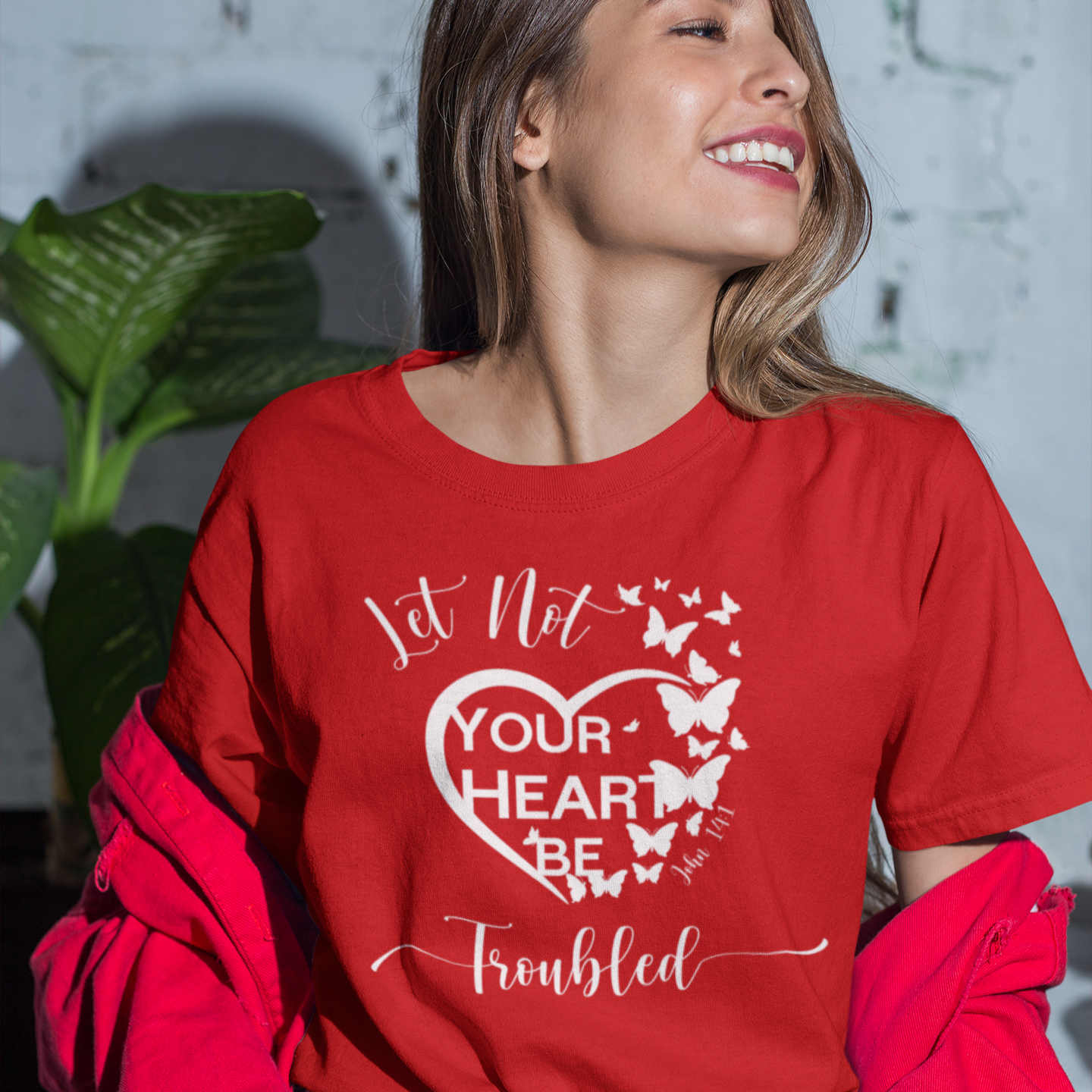 Woman wearing a red t-shirt with a motivational quote, standing indoors with plants in the background.