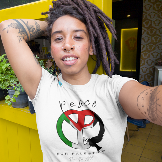 Person wearing a white t-shirt with a peace symbol design, sitting against a yellow wall with plants.