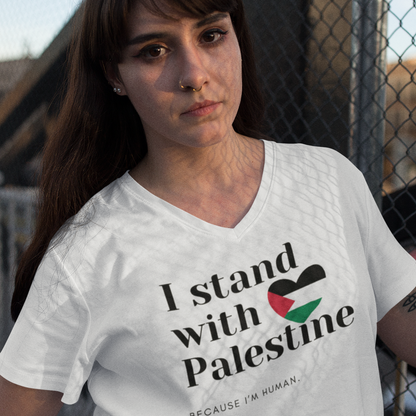 Person wearing a white t-shirt with 'I stand with Palestine' text, standing in front of a chain-link fence.