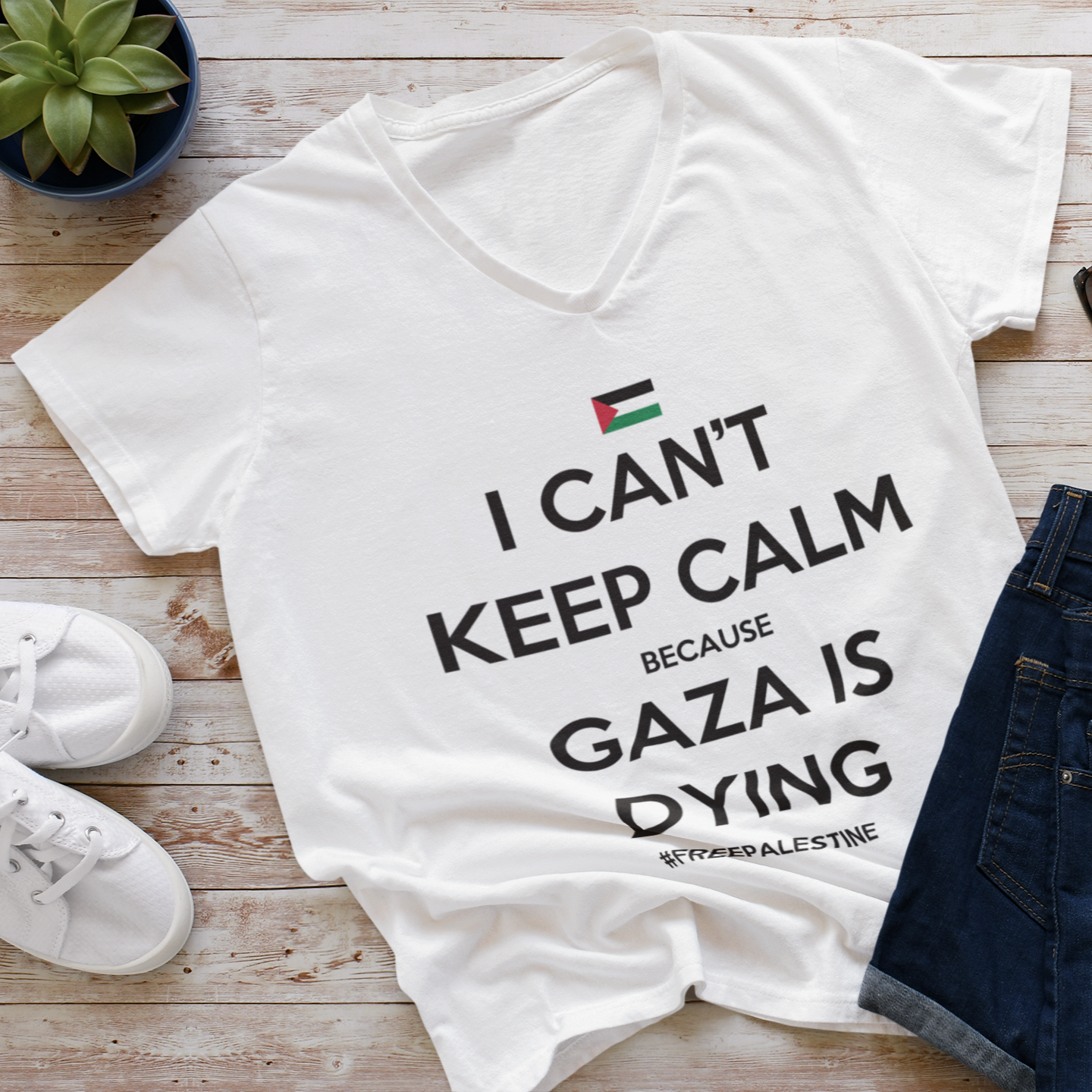 White t-shirt with 'I can't keep calm because Gaza is dying' text on a wooden surface with shoes and sunglasses.