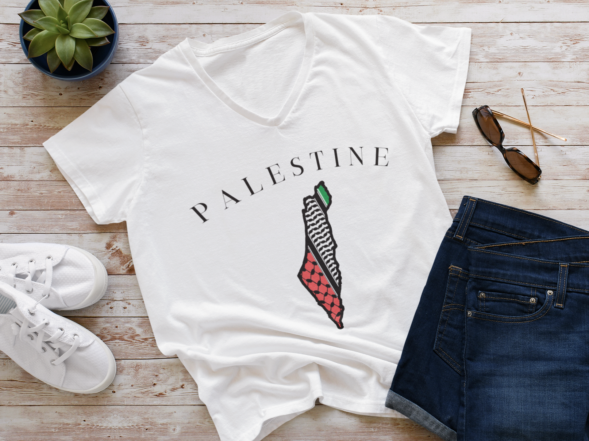 White t-shirt with 'PALESTINE' and map design on a wooden surface with shoes and sunglasses.