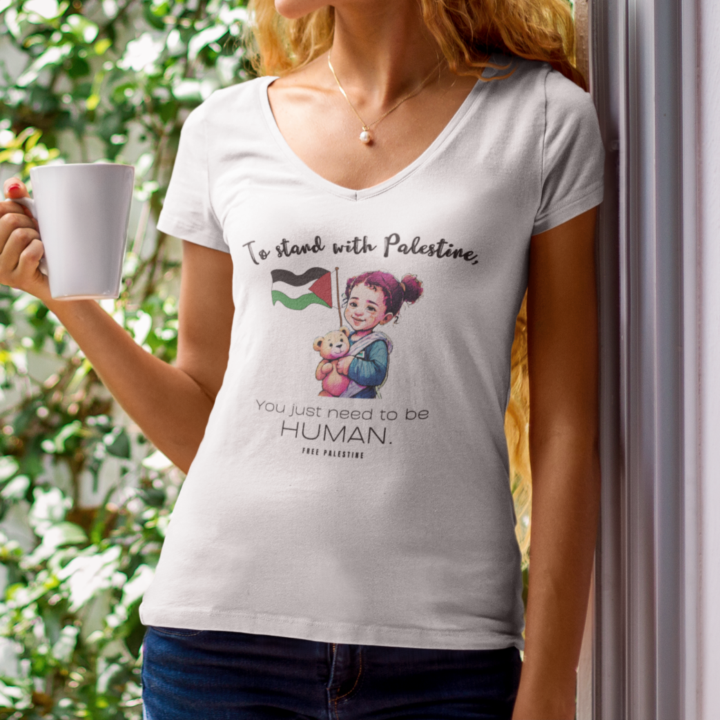 Woman wearing a t-shirt with a graphic design, holding a mug, standing in front of a green leafy background.